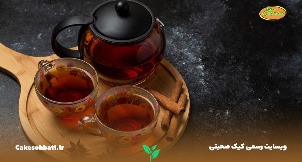 تصویری از نمای بالا و نزدیک که دو عدد لیوان از انواع چای و چند عدد چوب دارچین را در کنار یک قوری شیشه‌ای پر از چای را بر روی یک سینی چوبی گرد نشان می‌دهد.