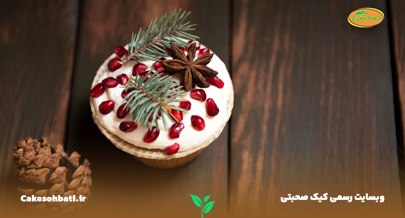 نمای نزدیک از یک کاپ کیک تزئین شده با انار و برگ درخت کاج در کنار یک کاج کوچک که به فروش فصلی کیک عمده و تائثیر فصول بر کیک‌ها دارد.