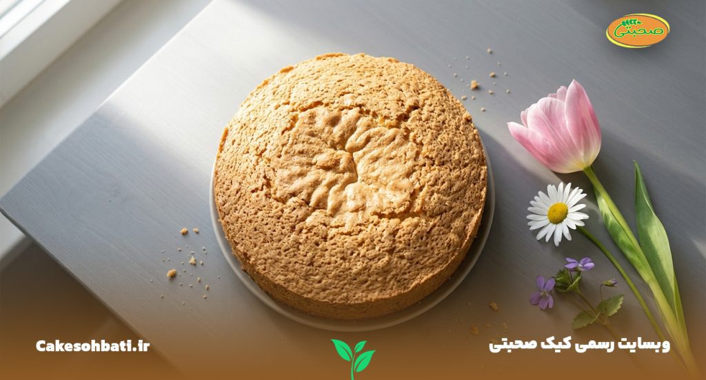 نمای بالایی از یک میز طوسی رنگ و چند عدد گل بهاری در کنار یک کیک اسفنجی بزرگ که به